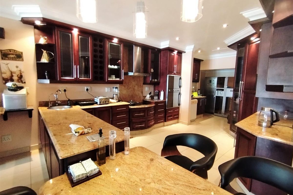 Spacious kitchen featuring dark wood cabinetry, granite countertops, integrated oven, extractor fan, and a breakfast bar island with tiled flooring.