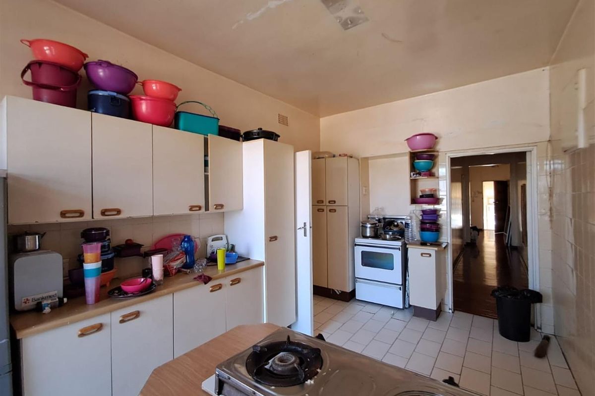 A dated kitchen featuring laminate cabinetry, tiled flooring, and a freestanding stove, requiring cosmetic updates to modernize the space.