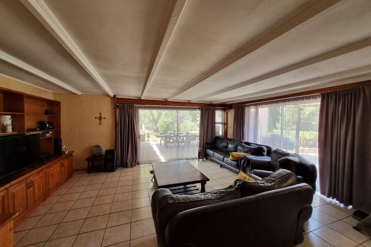 Spacious living room featuring tiled flooring, exposed beam ceiling, and large sliding glass doors providing direct access to the outdoor patio area.
