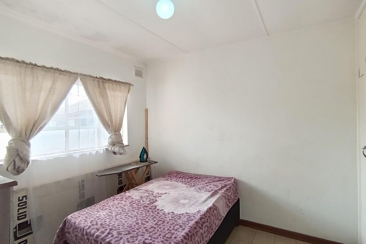 A simple bedroom featuring a window with curtains, tiled flooring, and a built-in cupboard.