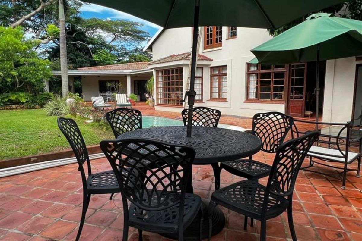 A spacious rear patio area featuring terracotta tiling, overlooking a swimming pool and the rear elevation of the residence.