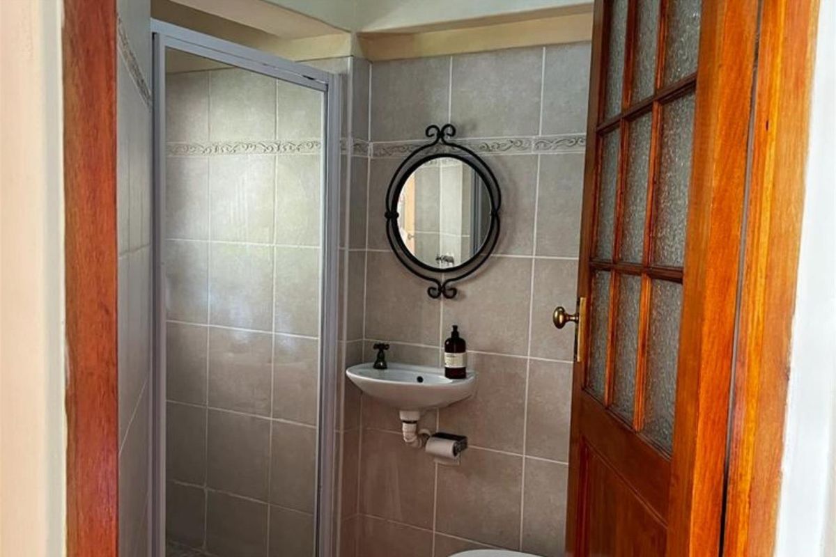 A compact bathroom featuring a tiled shower enclosure, a wall-mounted basin, and a decorative mirror, finished with neutral wall tiles.