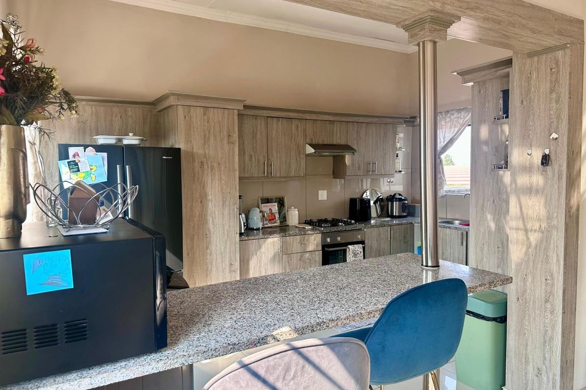 A functional kitchen featuring wood-look cabinetry, granite countertops, a breakfast bar, and built-in oven with gas hob and extractor fan.