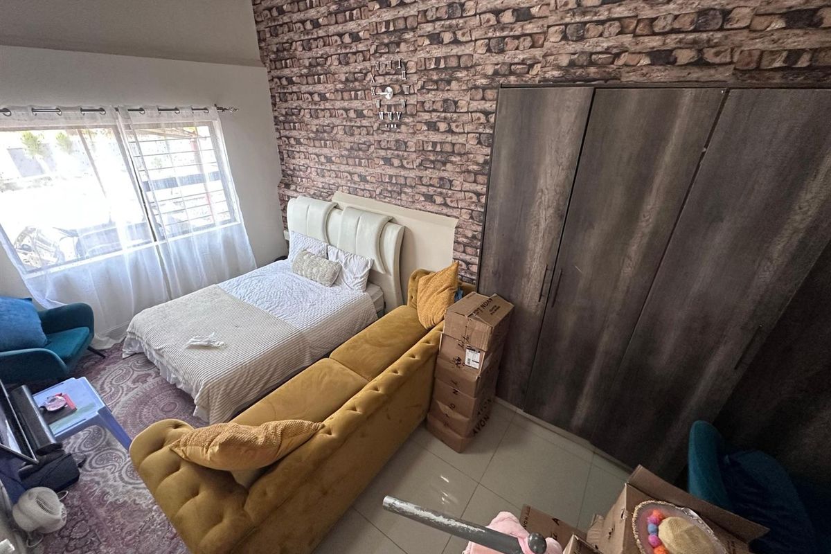 A bedroom featuring a brick-effect feature wall, built-in wardrobe, and tiled flooring, offering a functional living space with natural light.