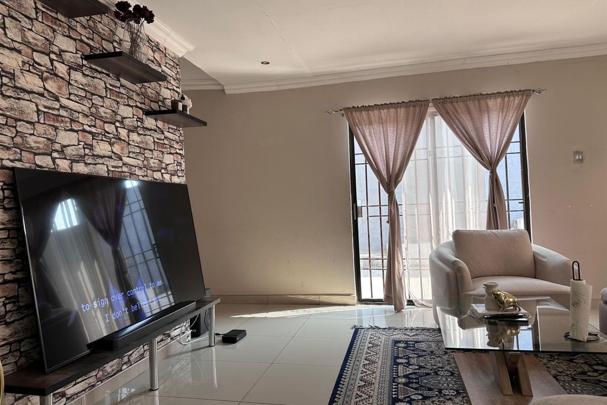 A bright living room featuring tiled flooring, a decorative stone-cladding feature wall, and sliding glass doors providing access to the exterior.