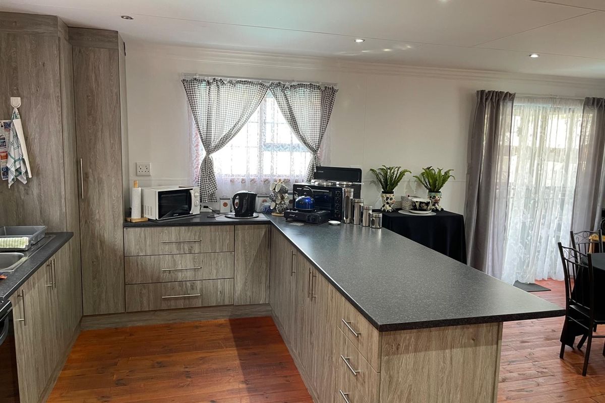 Modern kitchen featuring wood-grain cabinetry, dark laminate countertops, and a functional breakfast bar island, complemented by warm timber-look flooring and recessed ceiling lighting.