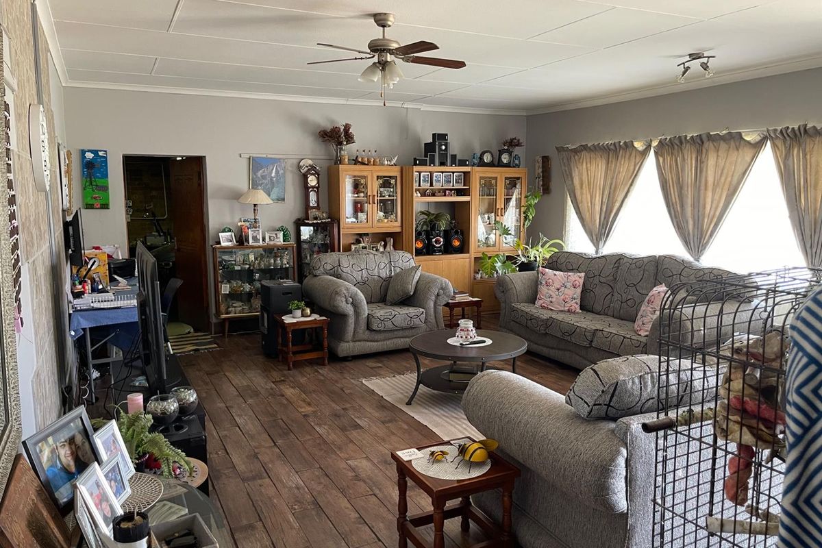 A spacious living room featuring dark wood-look flooring, a ceiling fan, and large windows that provide natural light to the living area.