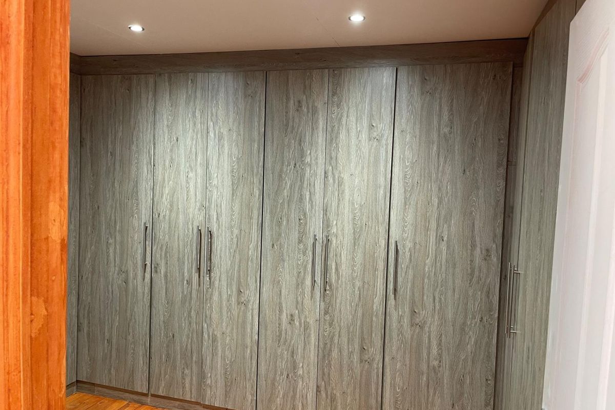 A bedroom featuring extensive floor-to-ceiling built-in wooden cabinetry with modern handles and recessed ceiling lighting.