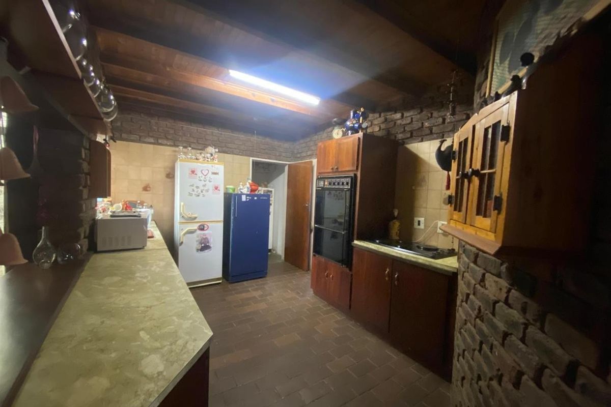 Rustic kitchen featuring exposed brick walls, timber beamed ceiling, tiled flooring, and built-in cabinetry with integrated oven and cooktop.