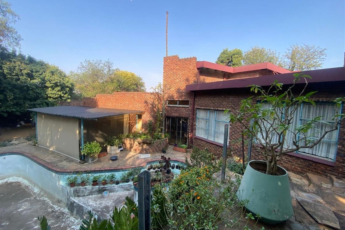 Rear exterior view featuring a brick facade, a swimming pool area, and a covered patio space set within a landscaped garden.