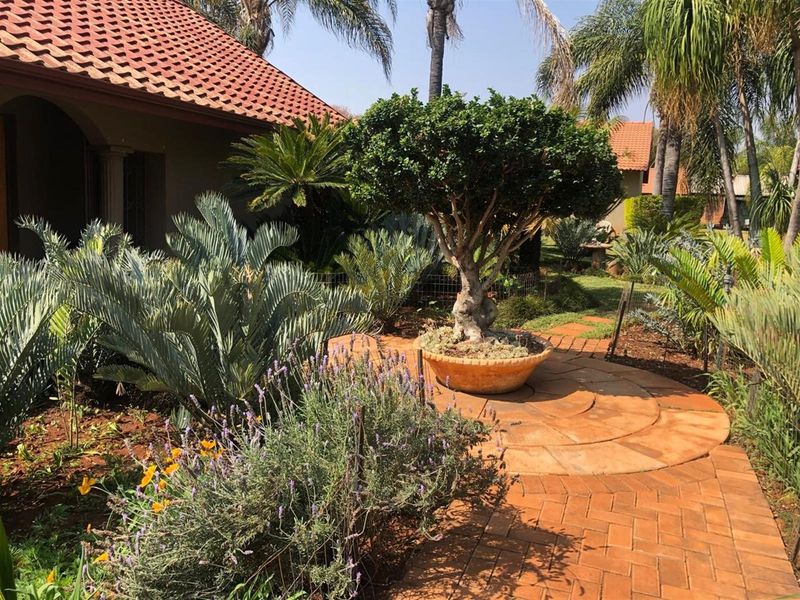 A well-maintained garden area featuring terracotta paving, mature landscaping, and a view of the property's clay-tiled roof structure.