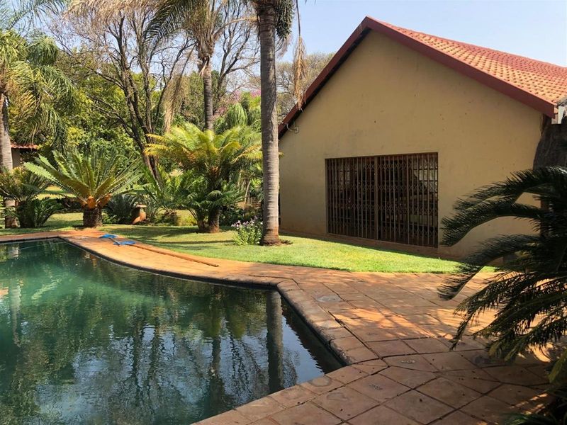 A view of the swimming pool area featuring a tiled deck, established garden surroundings, and a building exterior with a security gate.