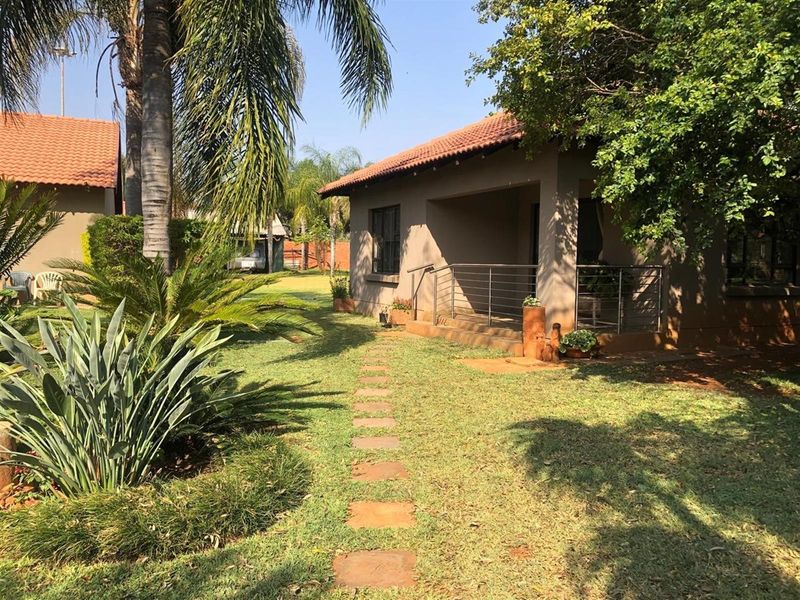 A well-maintained rear exterior view featuring a covered patio with stainless steel railings, a stone pathway, and established garden landscaping.