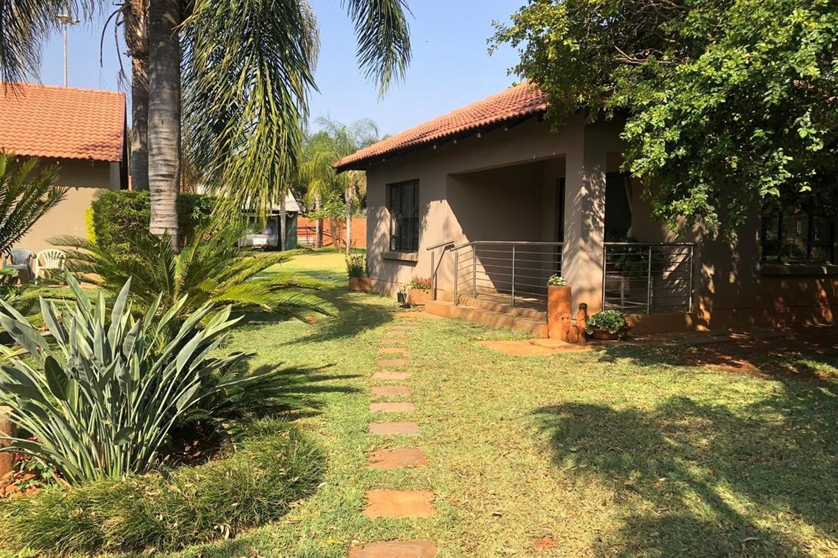 A well-maintained rear exterior view featuring a covered patio with stainless steel railings, a stone pathway, and established garden landscaping.