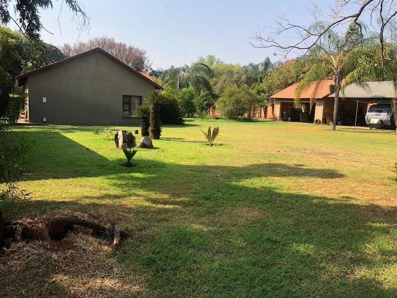 Spacious garden area featuring a well-maintained lawn, mature trees, and views of the property's outbuildings and main dwelling.