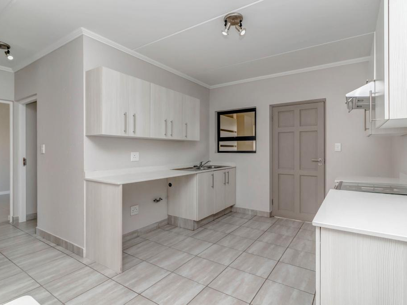 A clean, modern kitchen featuring light-toned built-in cabinetry, laminate countertops, a stainless steel sink, and tiled flooring, offering a bright and functional workspace.