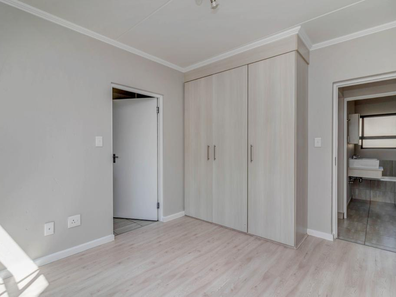 A bright, empty bedroom featuring light-toned laminate flooring, built-in cupboards, and direct access to an en-suite bathroom.