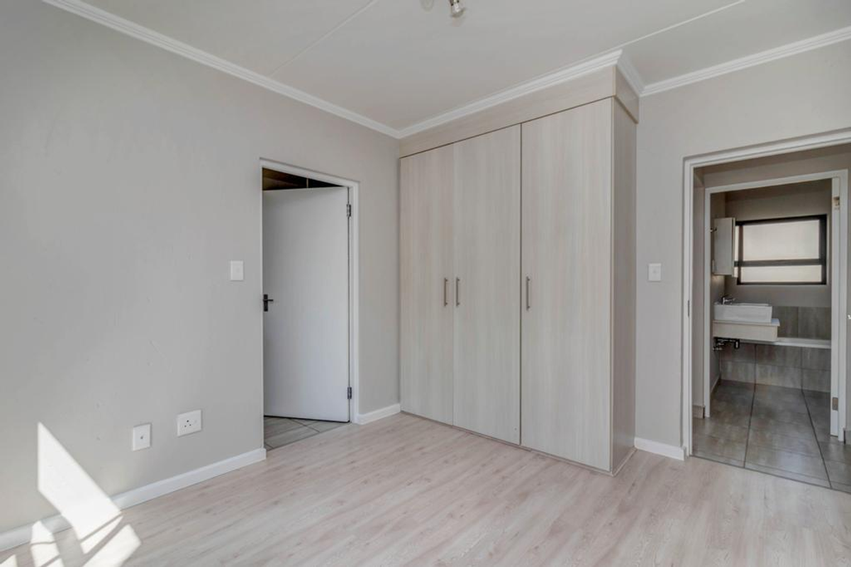 A bright, empty bedroom featuring light-toned laminate flooring, built-in cupboards, and direct access to an en-suite bathroom.