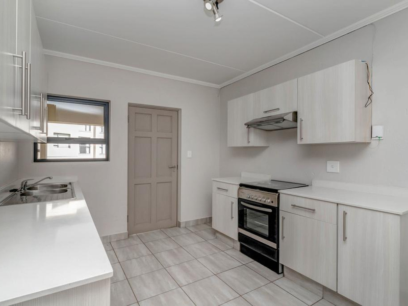 A functional kitchen featuring light-toned built-in cabinetry, a stainless steel sink, an electric stove with an extractor fan, and tiled flooring.