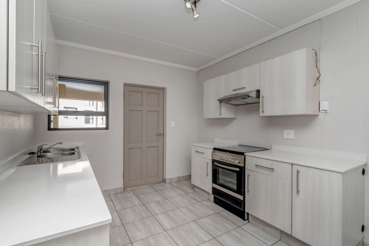 A functional kitchen featuring light-toned built-in cabinetry, a stainless steel sink, an electric stove with an extractor fan, and tiled flooring.