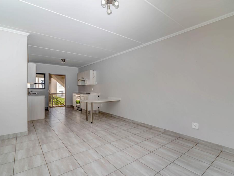 An open-plan living and kitchen area featuring tiled flooring, built-in cabinetry, and a breakfast counter, offering a clean and functional space.