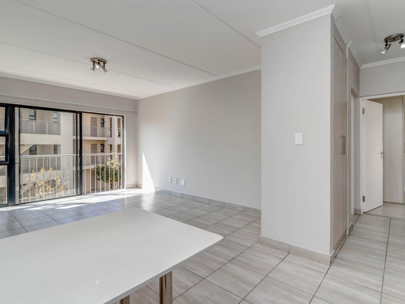 A bright, empty living area featuring neutral tiled flooring, a built-in cupboard, and a large sliding glass door leading to a balcony.