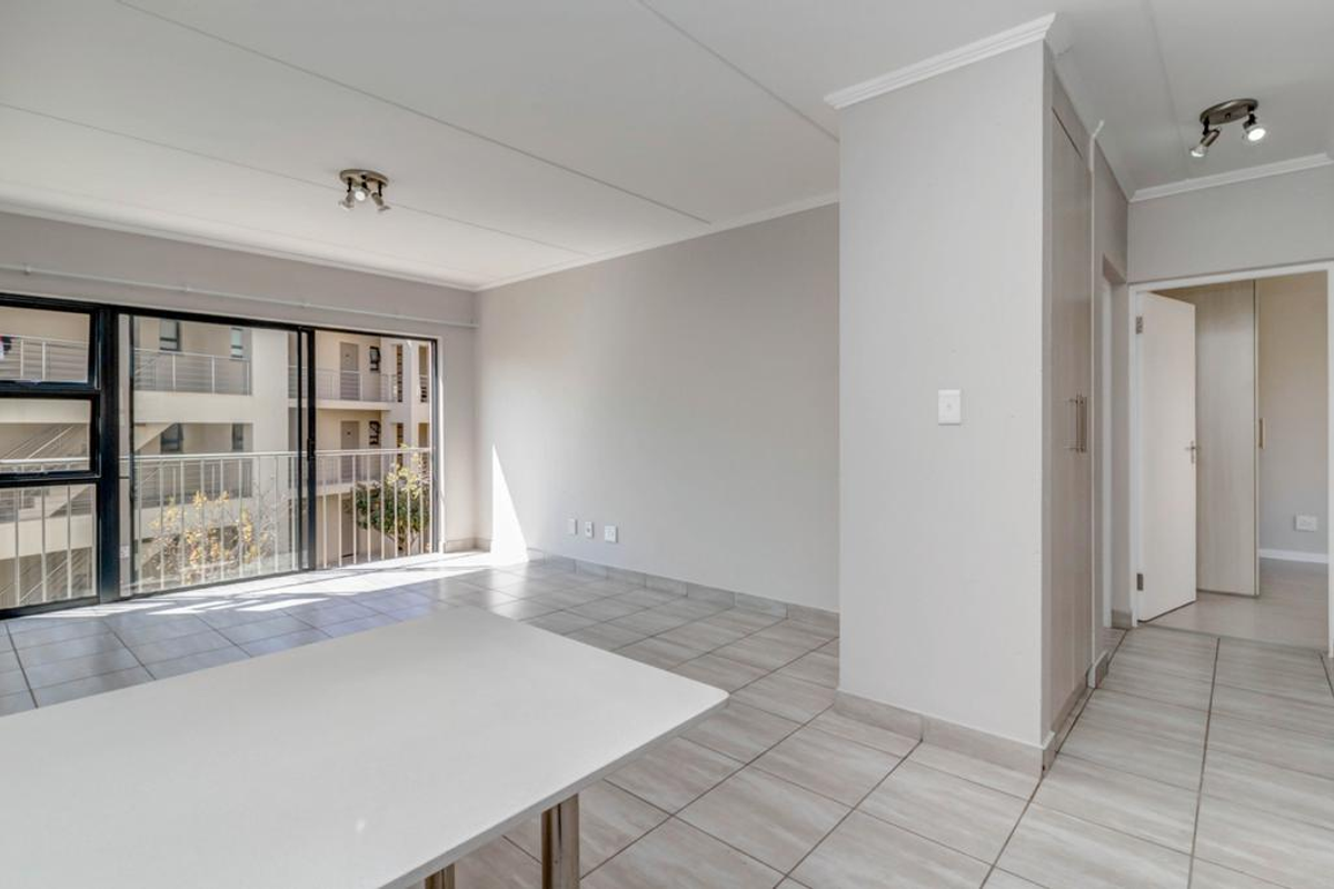 A bright, empty living area featuring neutral tiled flooring, a built-in cupboard, and a large sliding glass door leading to a balcony.