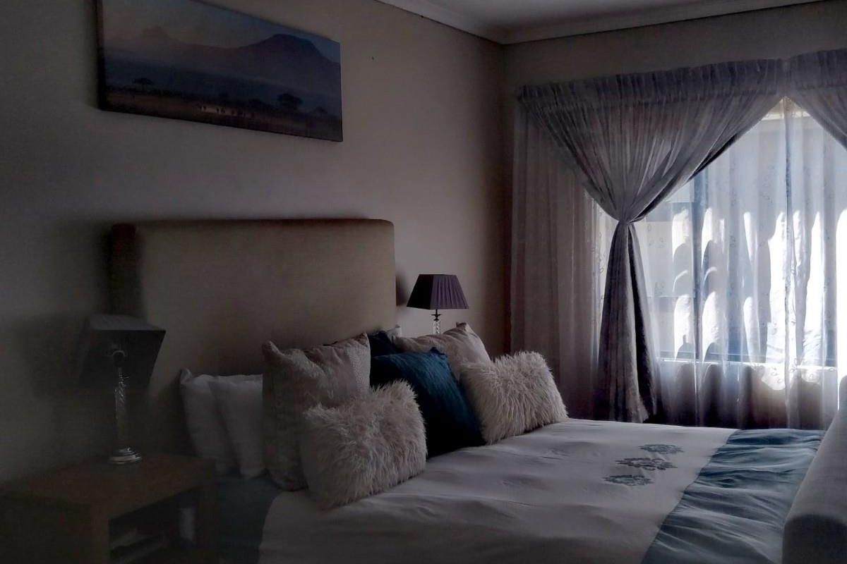 A cozy bedroom featuring a neutral color palette, soft natural lighting through window curtains, and a comfortable bed setup.