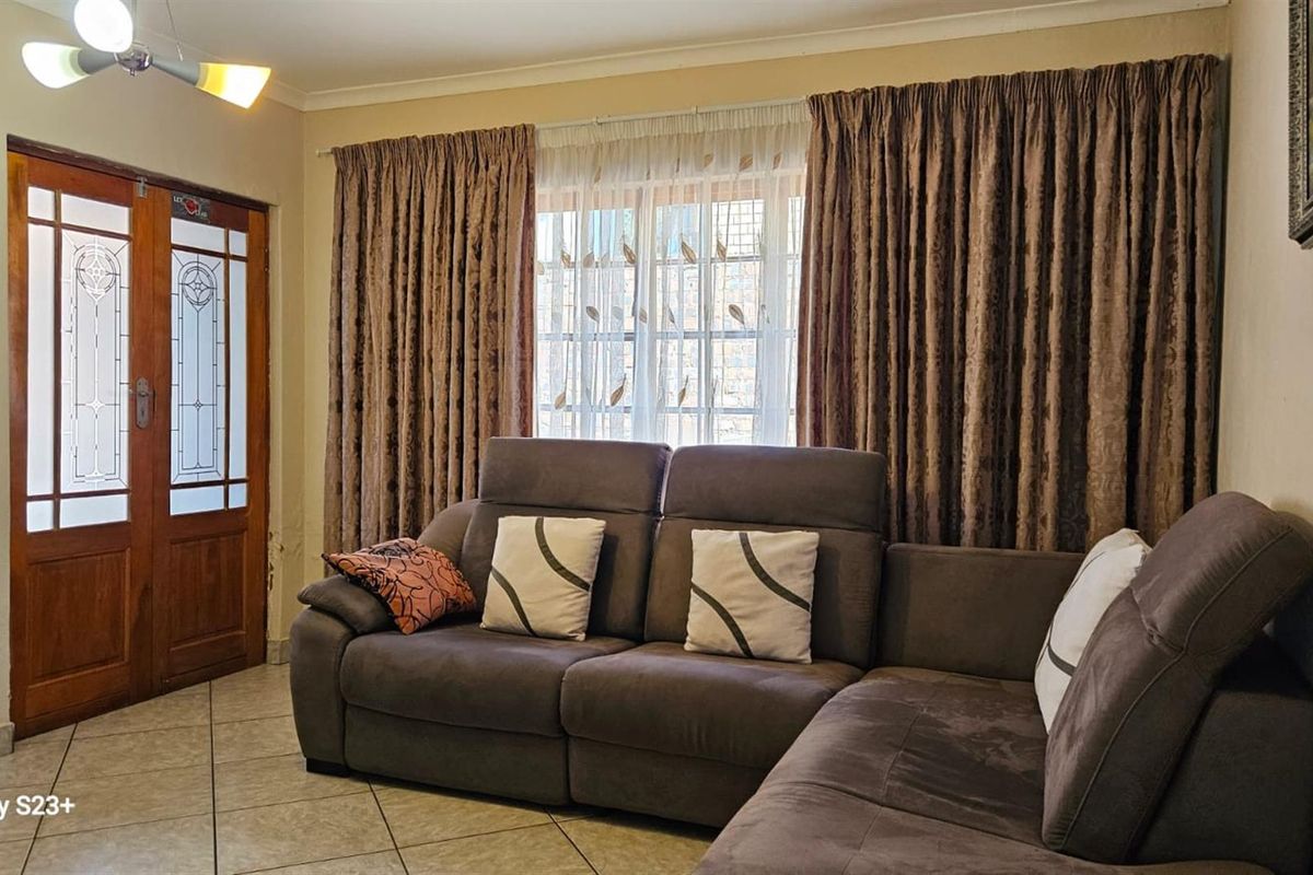 A living room featuring tiled flooring, a wooden framed glass door, and large windows with curtains.