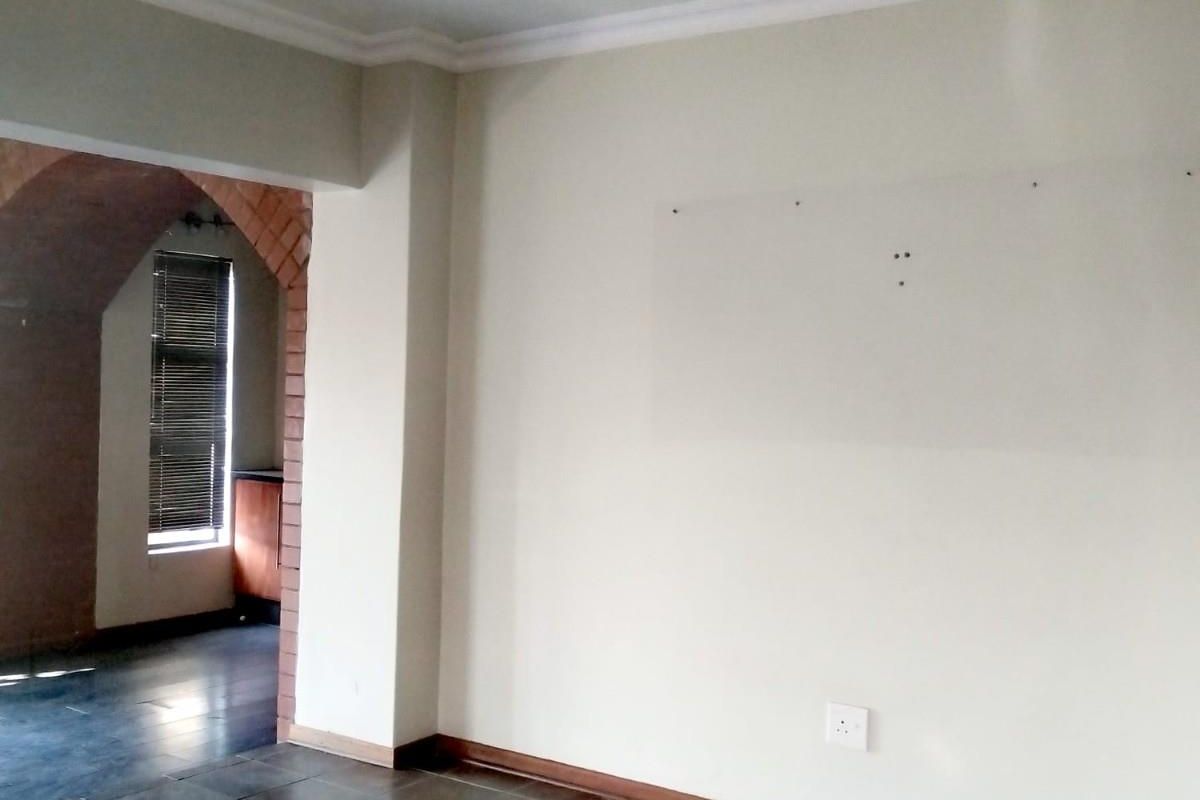 An empty living area featuring tiled flooring, crown molding, and an arched entryway leading to an adjacent space with window blinds.