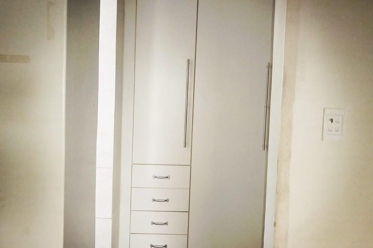 A built-in bedroom cupboard featuring white cabinetry with integrated drawers and vertical handles.