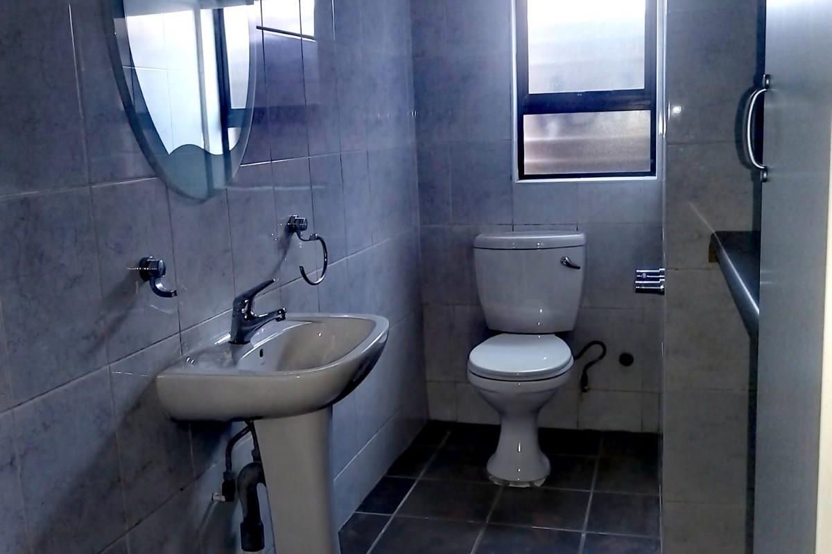 A functional bathroom featuring a pedestal basin, toilet, and tiled walls and flooring, providing a clean and practical space.