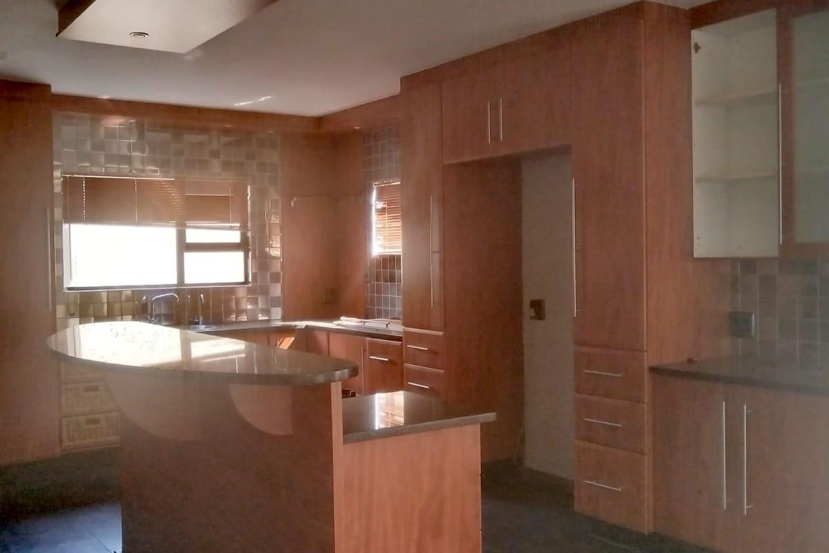A spacious kitchen featuring wood-finish cabinetry, a breakfast bar with stone countertops, tiled splashbacks, and a recessed ceiling feature with integrated lighting.
