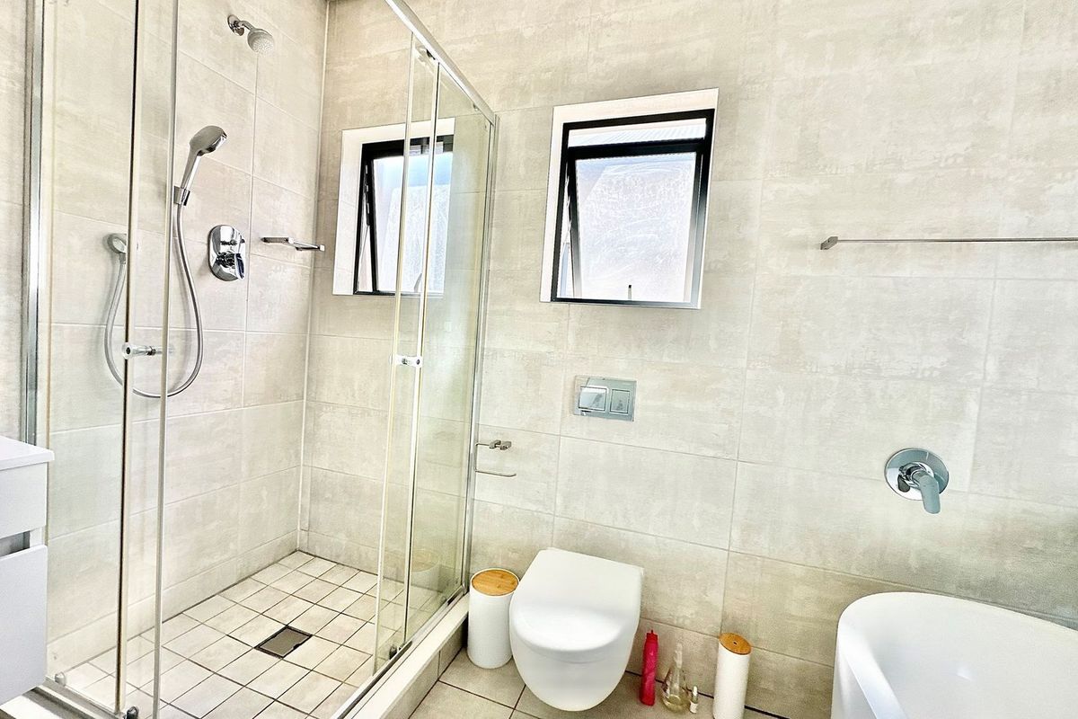 Modern bathroom featuring a glass-enclosed walk-in shower, wall-mounted toilet with concealed cistern, and neutral floor-to-ceiling tiling.