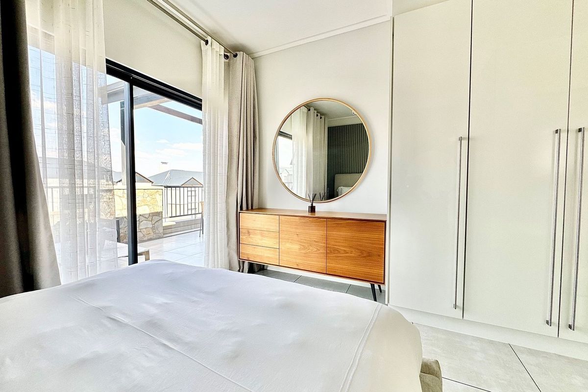 A bright bedroom featuring built-in floor-to-ceiling wardrobes, tiled flooring, and large sliding glass doors providing direct access to a private balcony.