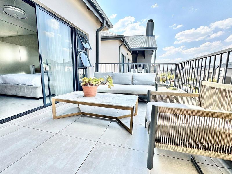 A spacious balcony featuring modern tiled flooring, black metal railings, and large sliding glass doors providing seamless access to the interior bedroom.