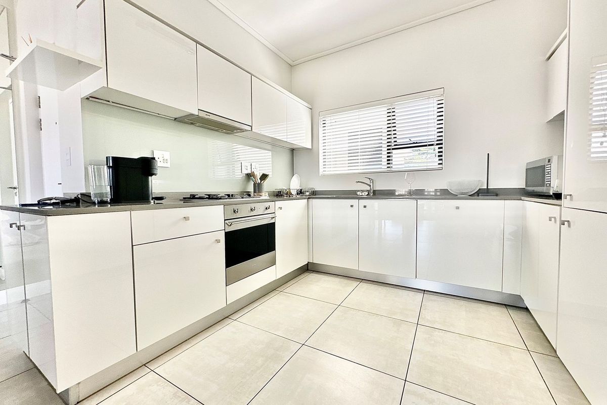 Modern kitchen featuring high-gloss white cabinetry, stone countertops, integrated stainless steel oven, gas hob, and tiled flooring.