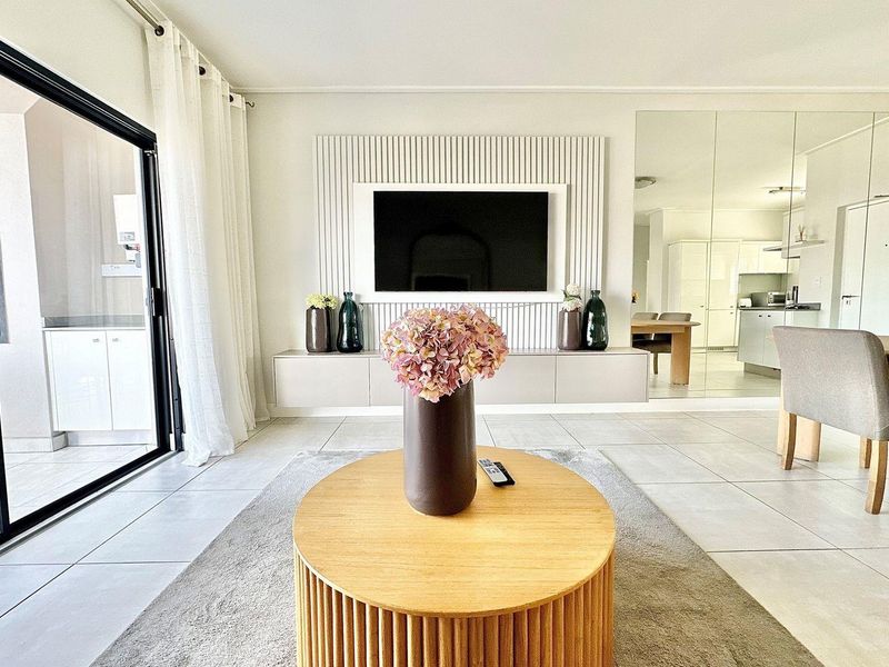 Modern open-plan living area featuring a sleek wall-mounted media unit, large format floor tiles, and seamless access to the outdoor patio.