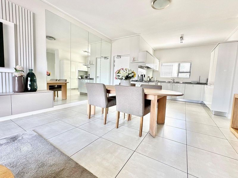 Modern open-plan living and dining area featuring large format floor tiles, a sleek kitchen with integrated cabinetry, and a large feature mirror wall.