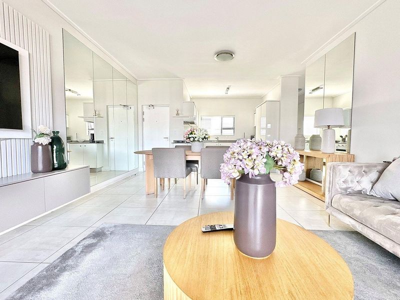 Open-plan living and dining area featuring tiled flooring, mirrored wall panels, and a modern kitchen visible in the background.