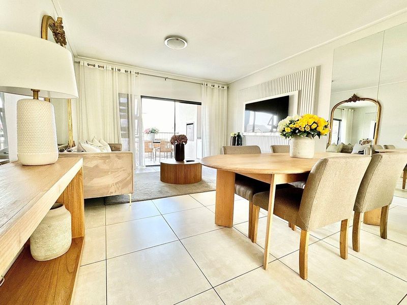 Bright open-plan living and dining area featuring large format floor tiles, a feature wall with integrated television mount, and sliding doors leading to a balcony.