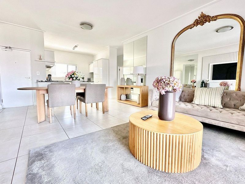Bright open-plan living and dining area featuring neutral floor tiles, modern kitchen cabinetry, and a mirrored feature wall.