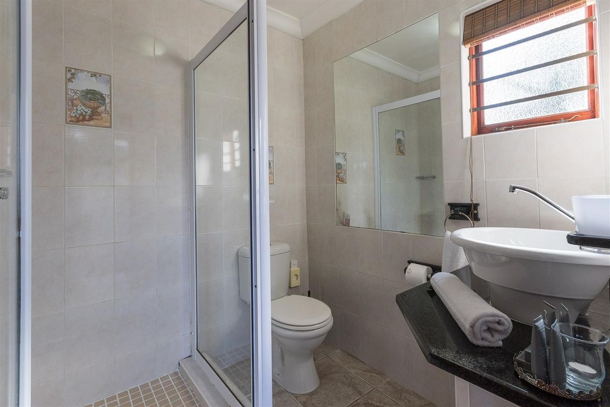 Compact bathroom featuring a glass-enclosed shower, a modern vessel sink on a granite vanity top, and neutral wall tiling.
