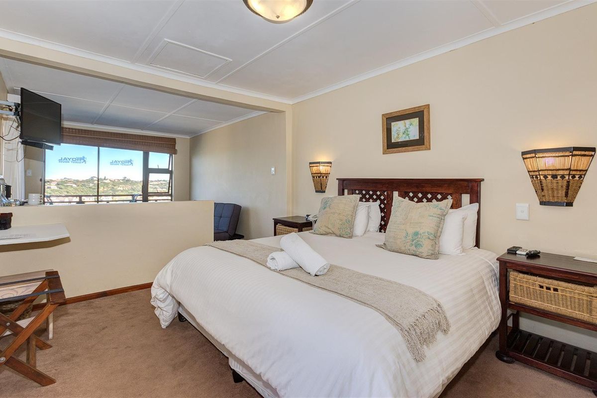 A comfortable bedroom featuring a split-level layout with an elevated seating area, large windows, and neutral wall finishes.