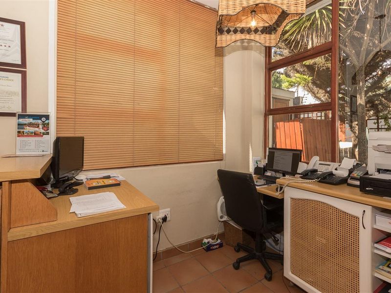 A functional office space featuring tiled flooring, built-in cabinetry, and large windows with wooden blinds, suitable for administrative use.