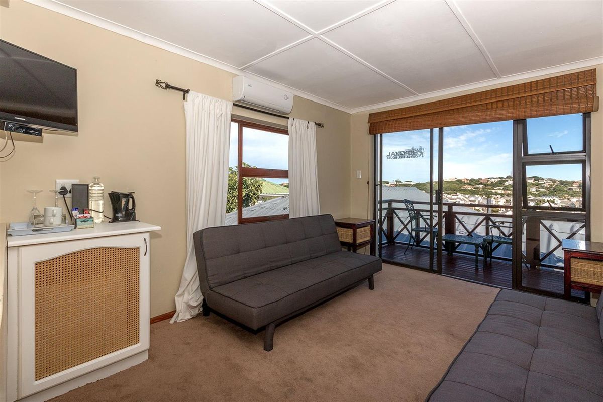 A comfortable living room featuring a wall-mounted air conditioning unit, sliding glass doors leading to a balcony, and views of the surrounding area.