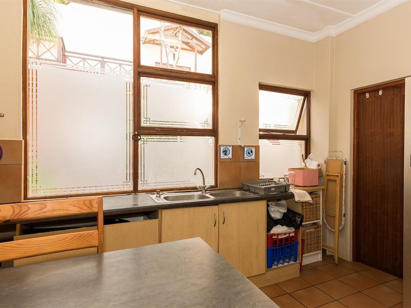 A functional scullery area featuring a double sink, laminate countertops, wooden cabinetry, and tiled flooring with natural light from large windows.