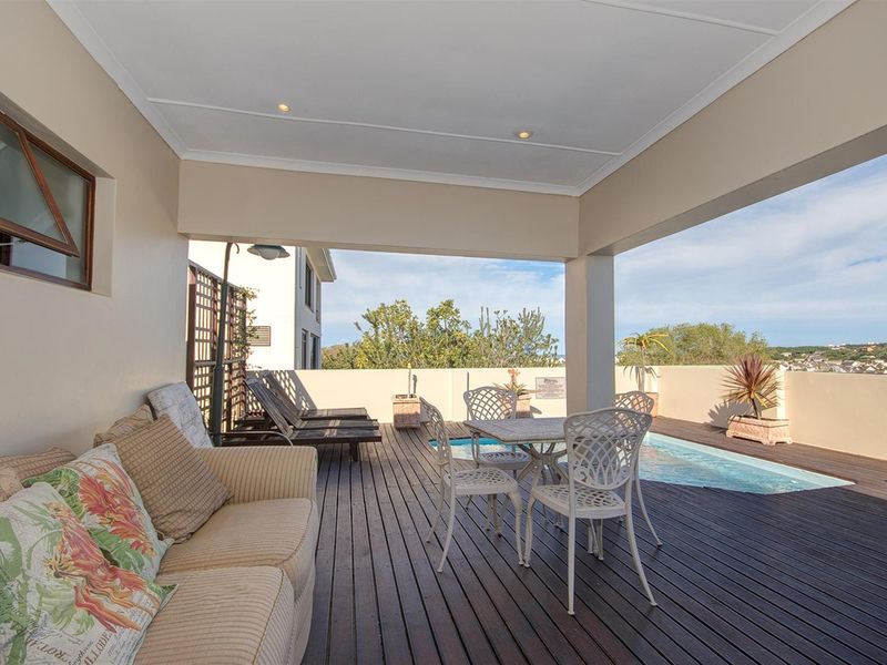 A covered patio area featuring timber decking, recessed ceiling lighting, and direct access to a private swimming pool with scenic views.