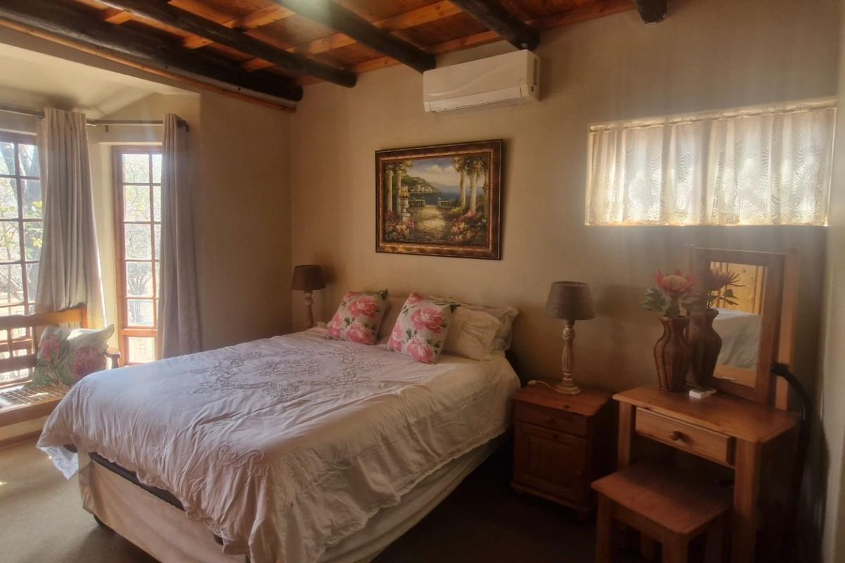 A cozy bedroom featuring exposed timber ceiling beams, a wall-mounted air conditioning unit, and large windows allowing for natural light.