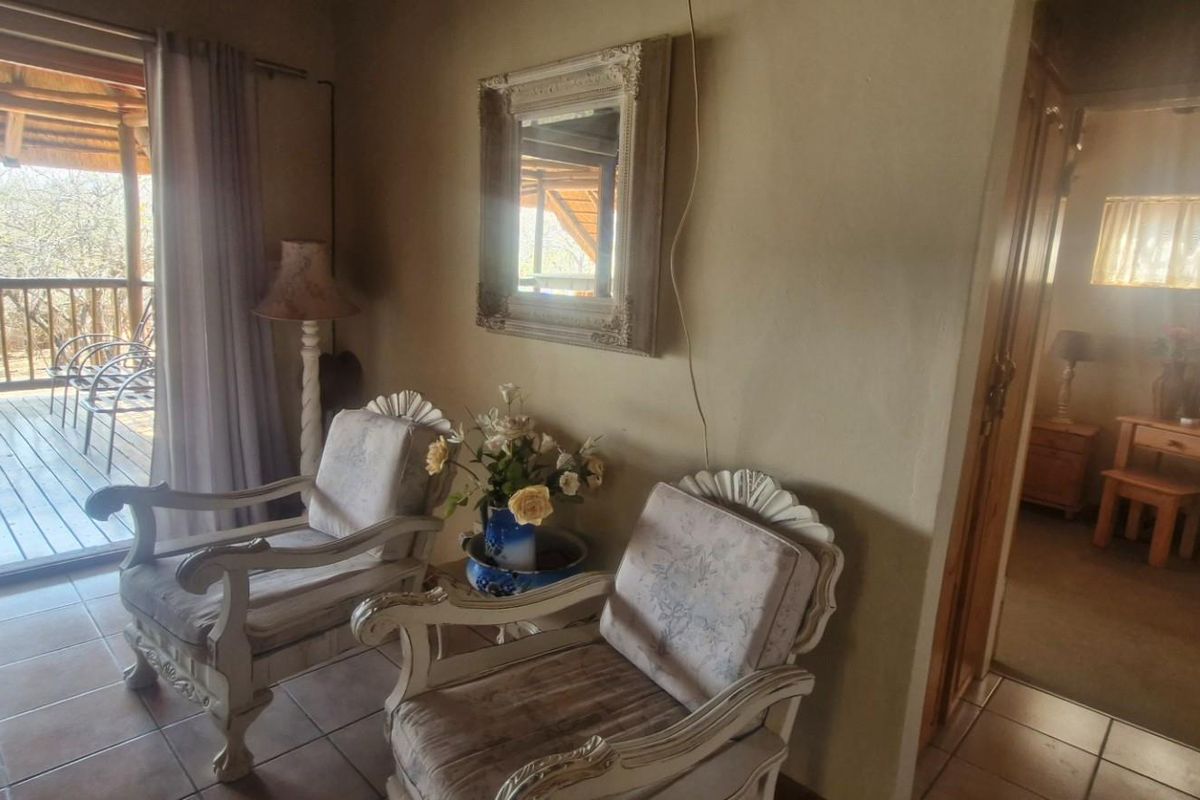 A living area featuring tiled flooring and direct access to a covered wooden deck, with an adjacent hallway leading to a bedroom.